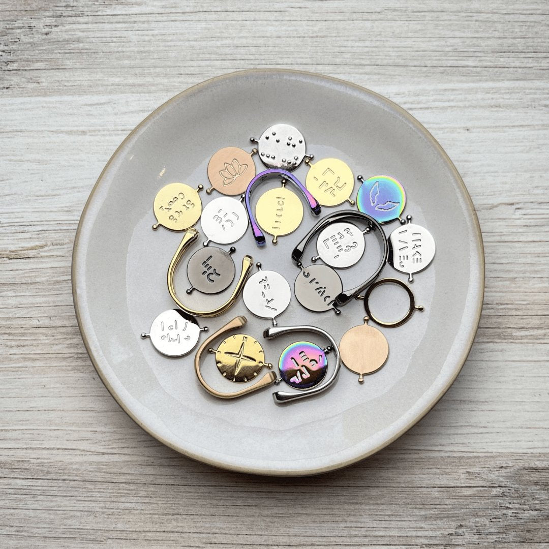 silver, gold, rose gold, black, and rainbow conquerings in a cream dish