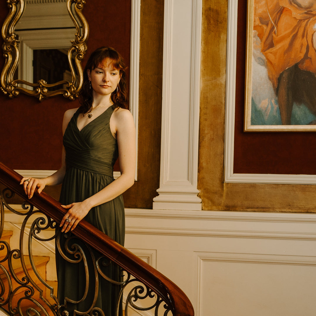 Person standing on a grand stair case wearing a green gown and fidget jewelry