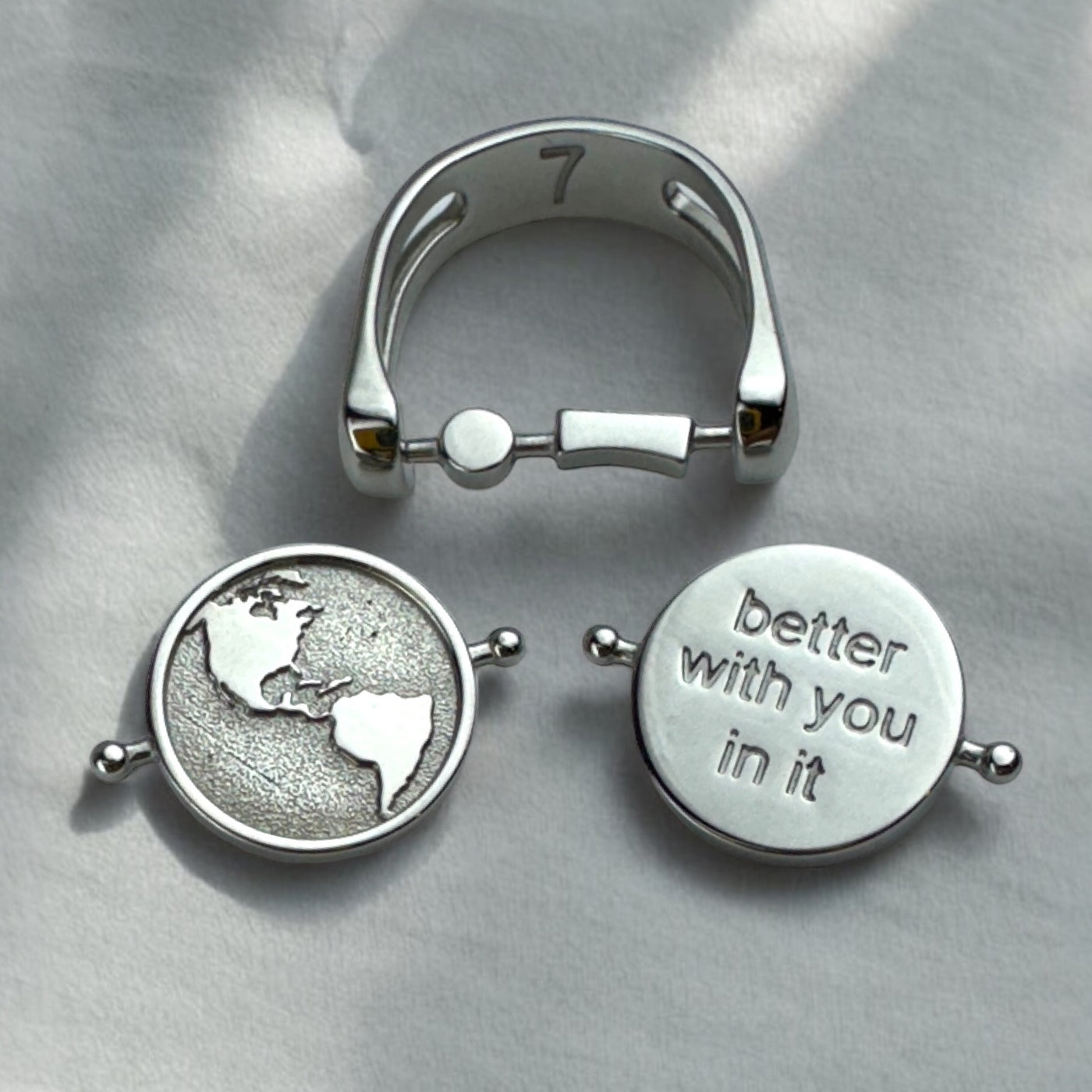 Fidget ring with a semicolon cross bar, an element with an etched globe, and an element with the phrase better with you in it