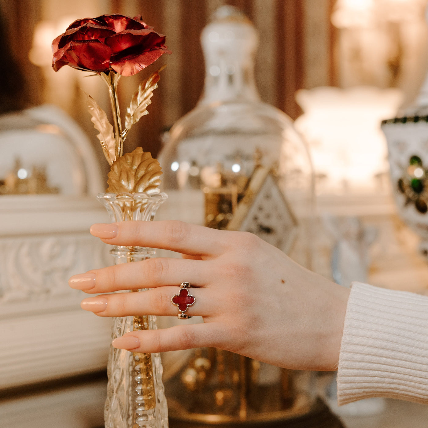 Person wearing a red quatrefoil fidget ring reaching for a red rose