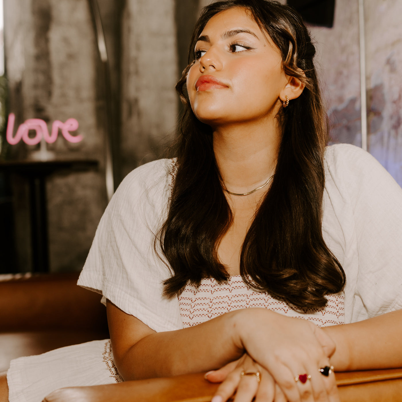 Person wearing a pink dress and heart-shaped fidget jewelry in front of a "love" neon pink sign