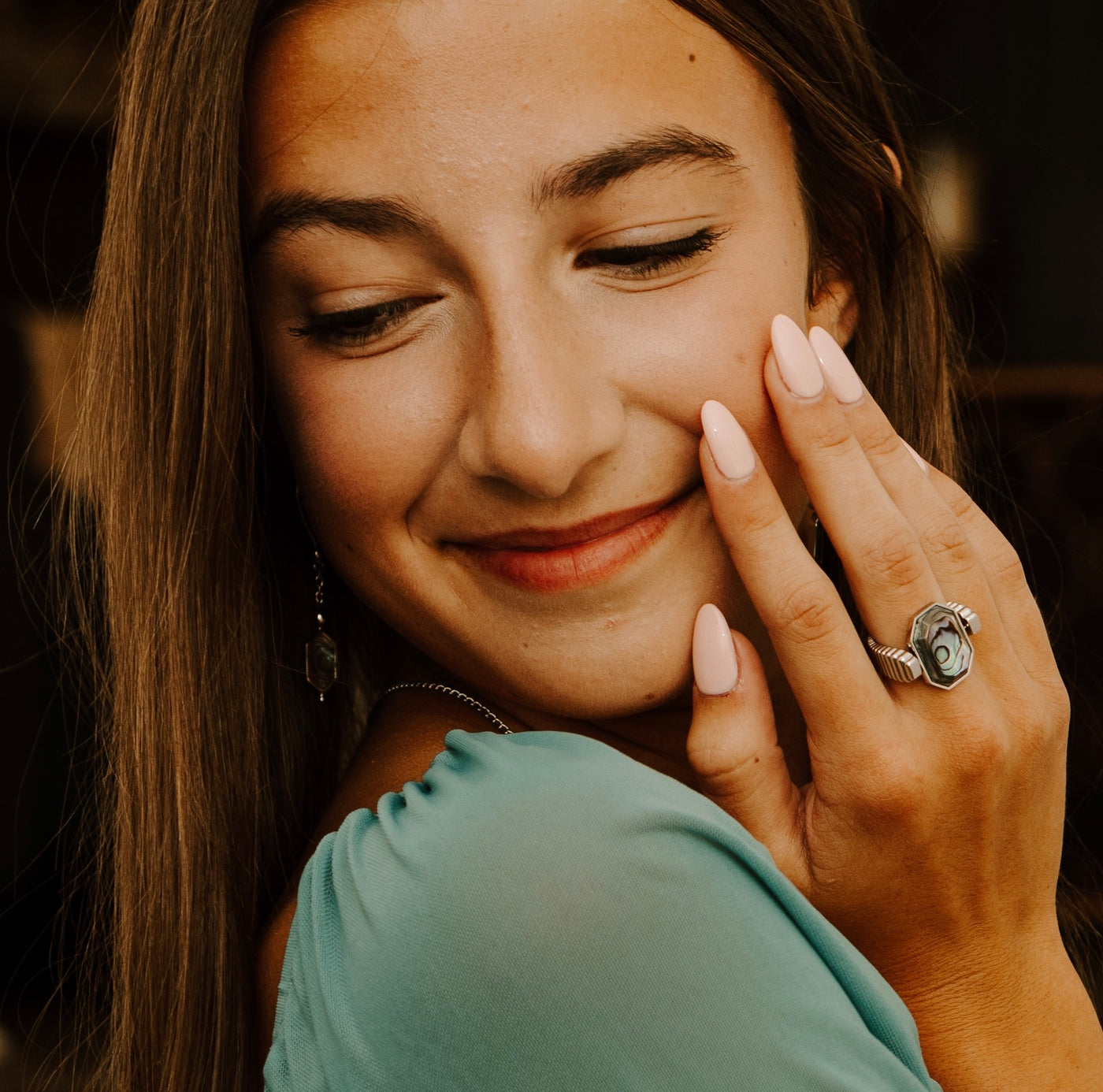 Person looking over their shoulder with their hand touching their face. They are wearing an Abalone Shell fidget ring