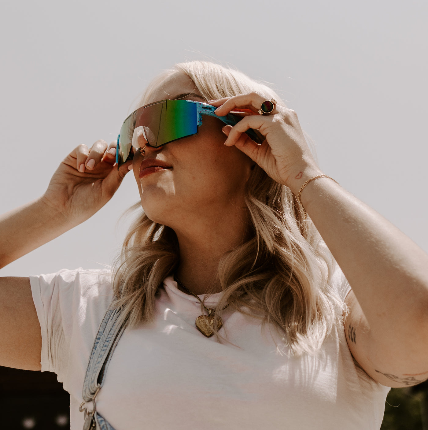 Person wearing holographic sunglasses looking up to the sky wearing fidget ring