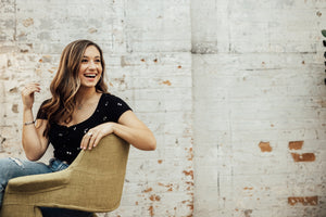 young woman sitting sideways in tan chair, laughing as she looks off camera